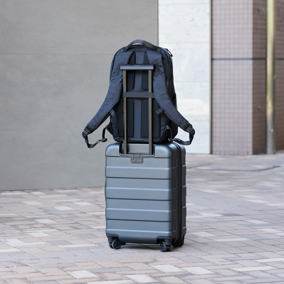 Gray suitcase with a backpack on top in an outdoor setting