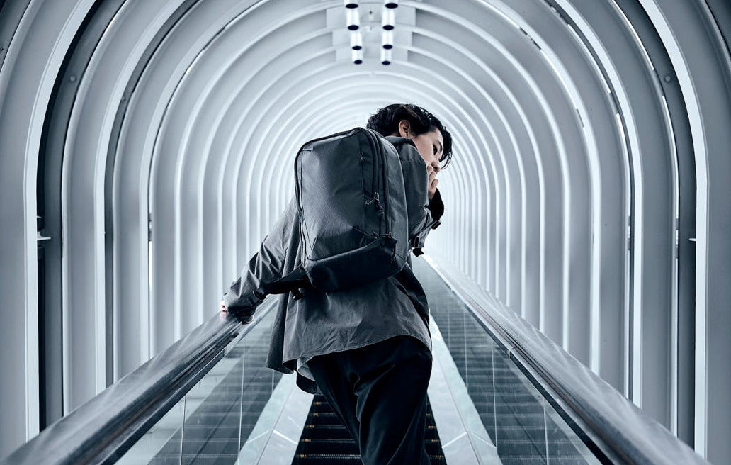 Person with a backpack ascending an escalator in a modern architectural setting
