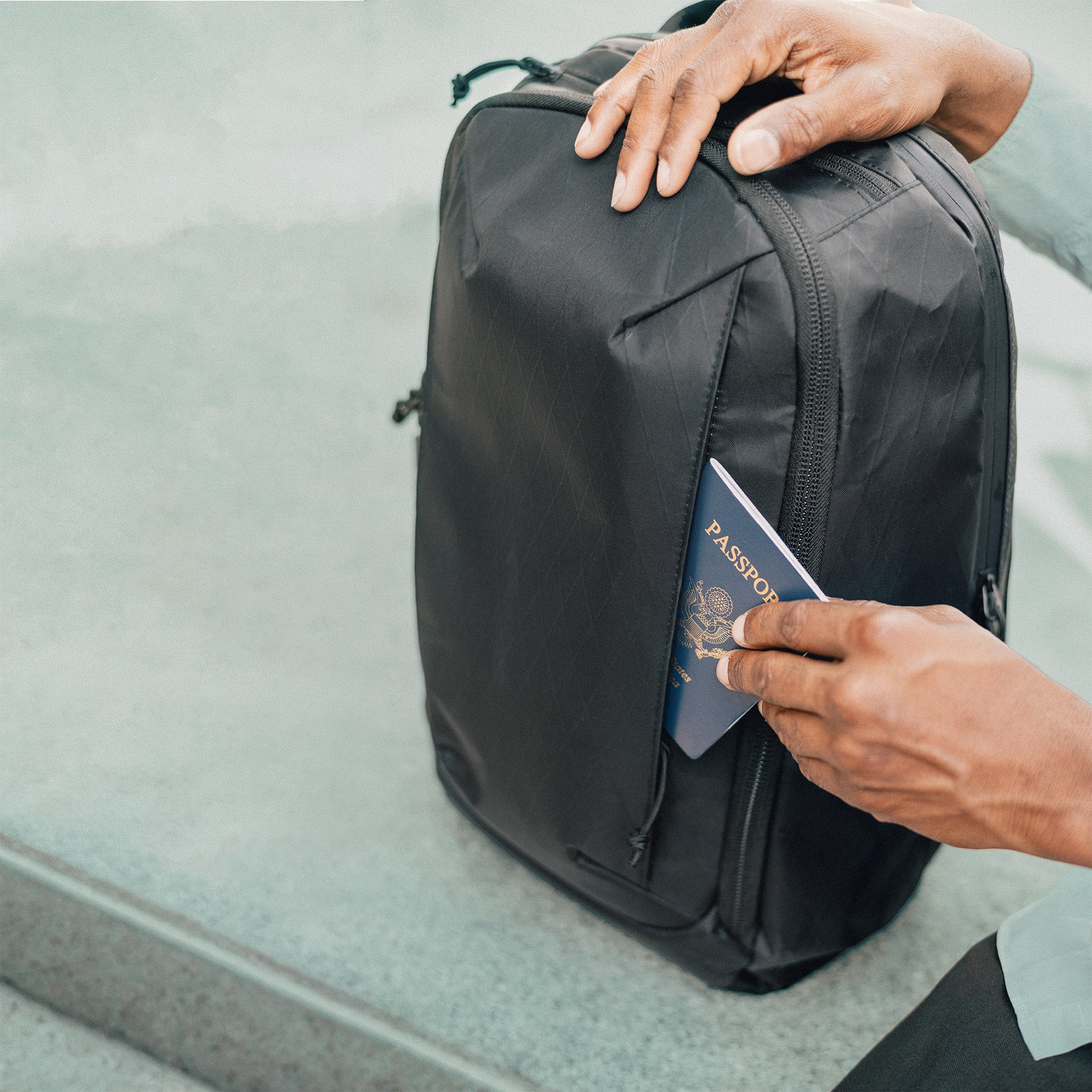 Person holding a black backpack and a passport on a light gray surface