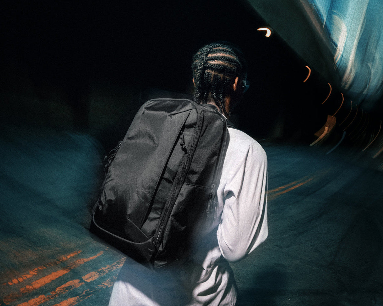 Person with a backpack walking through a dark, abstract tunnel.